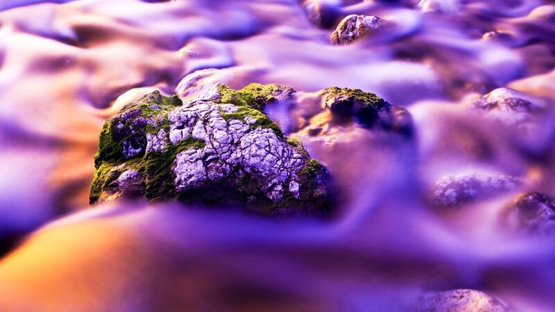 Purple water flowing over mossy rocks