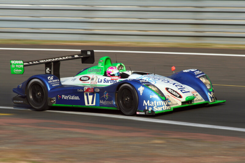 Racing Car on Track — Blue, Dynamic, Afternoon, Photograph, Driver, Race Car, Safety Barrier