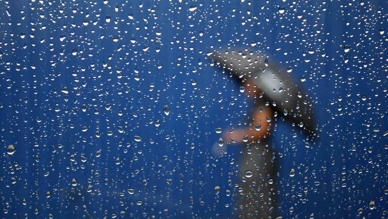 Raindrops on a window with a person holding an umbrella