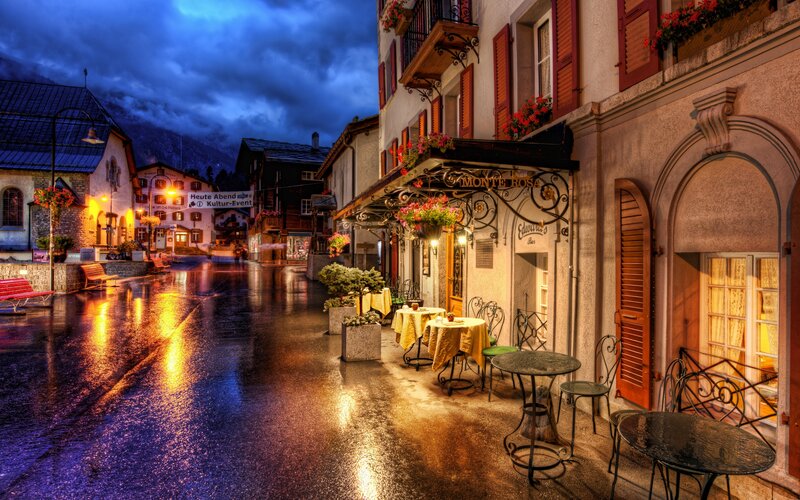 Rainy Street Cafe — Blue, Dramatic, Night, Photograph, Buildings, Tables, Mountains
