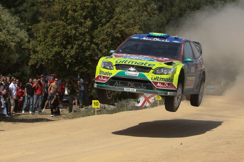 Rally Car in Mid-air — Green, Dynamic, Afternoon, Photograph, Crowd, Trees