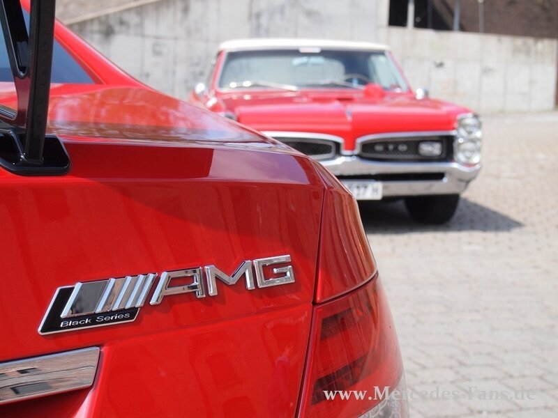 Red AMG car with classic car in background