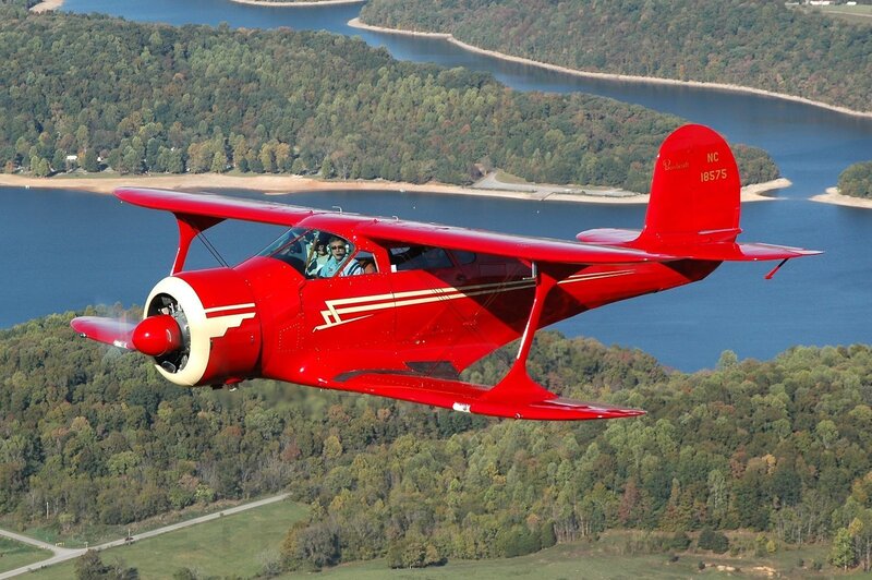 Red biplane flying over a river