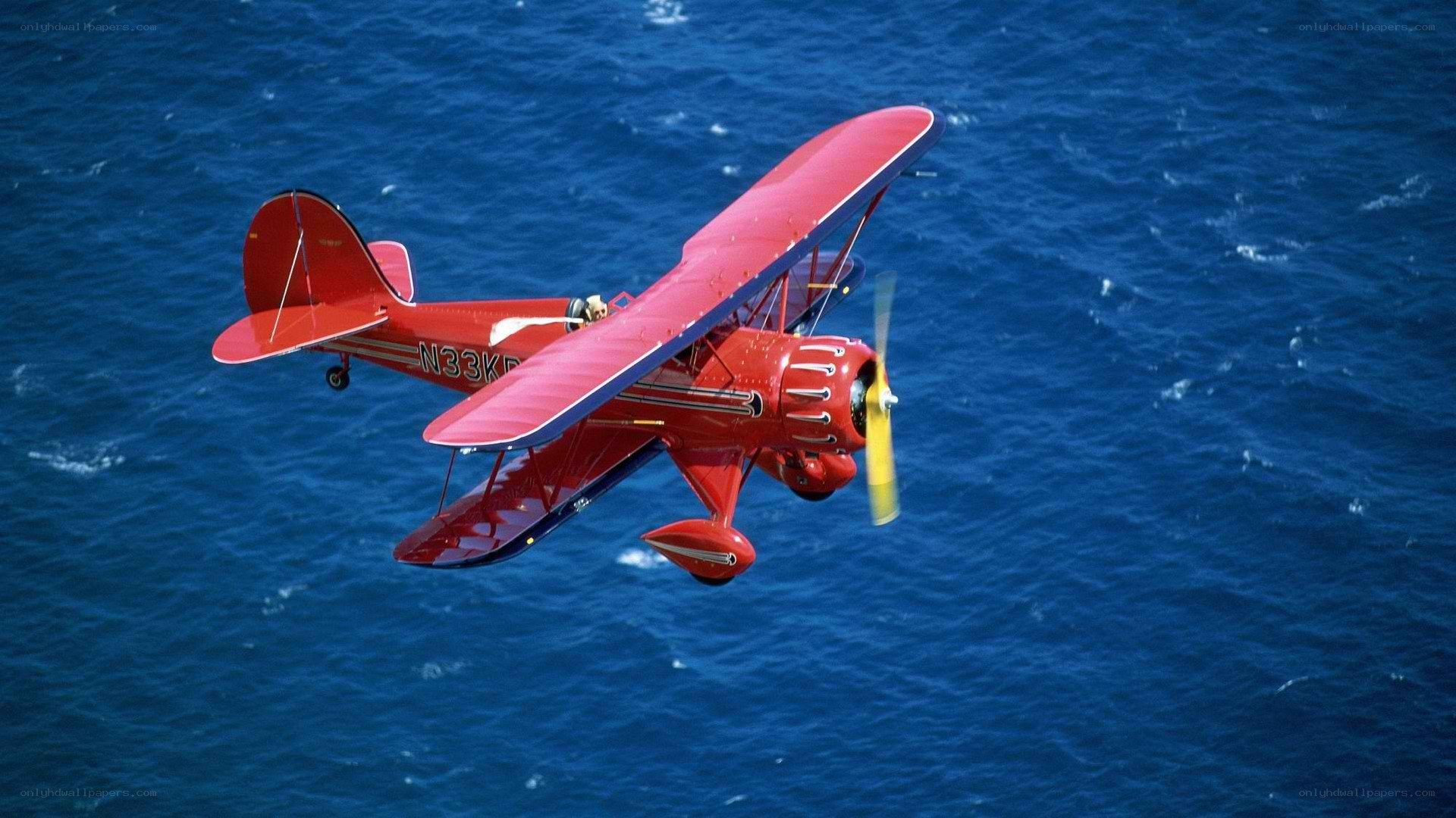 Red biplane flying over ocean