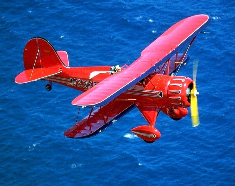 Red biplane flying over ocean