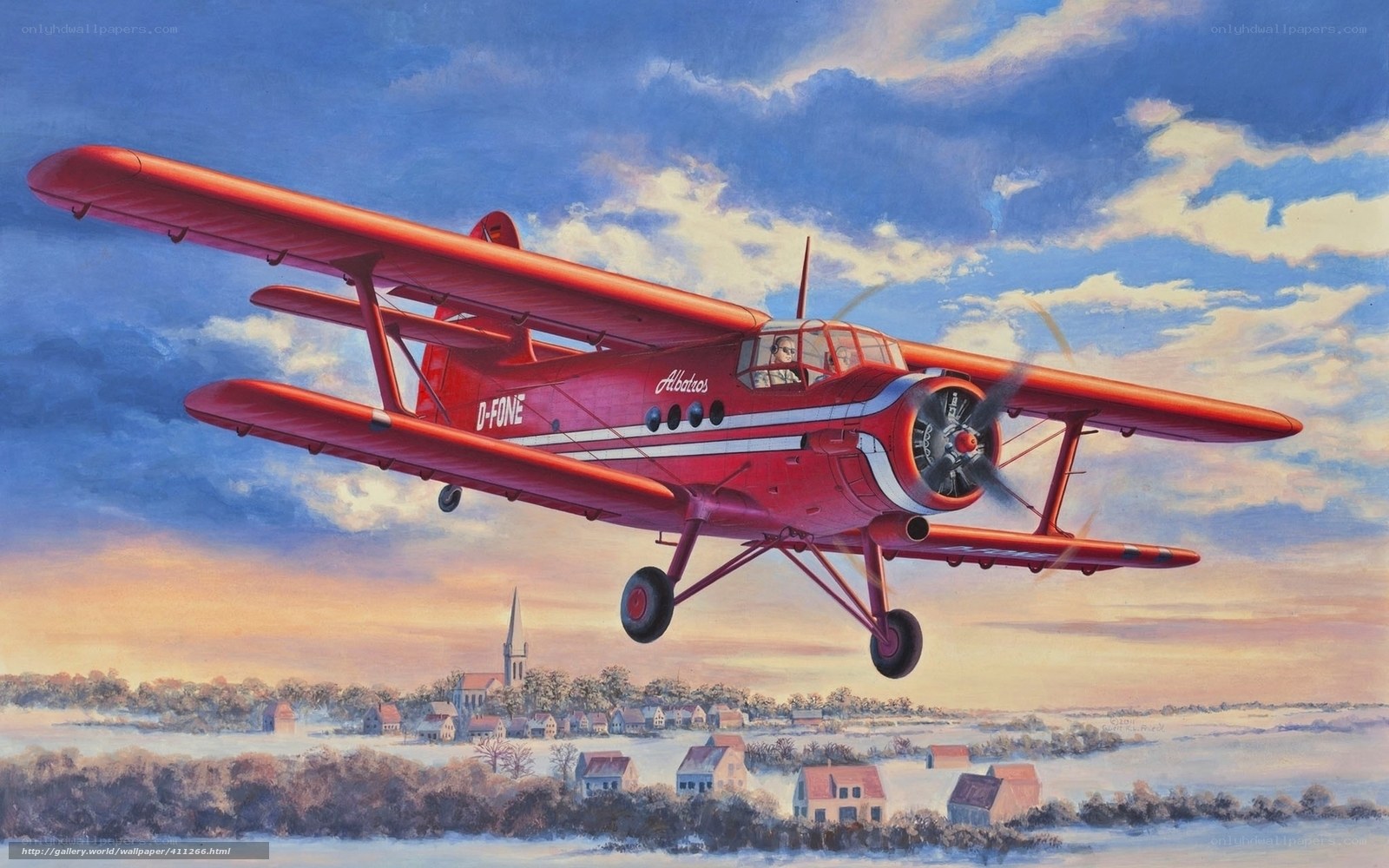 Red biplane flying over village