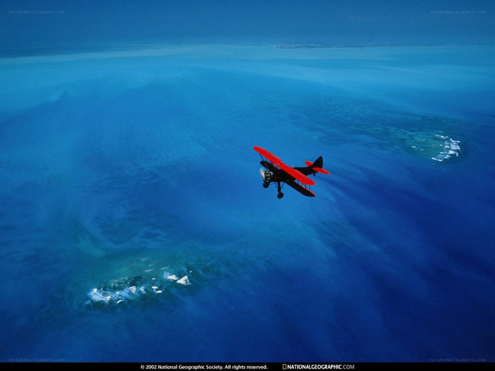 Red biplane over blue ocean