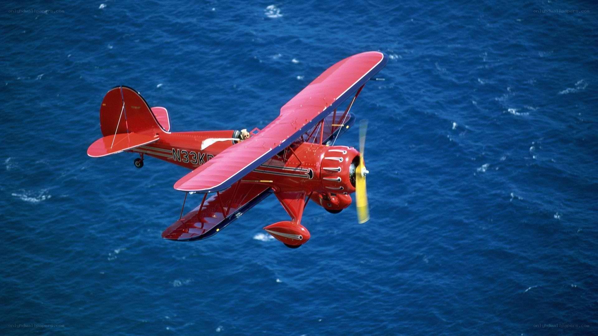 Red biplane over blue ocean