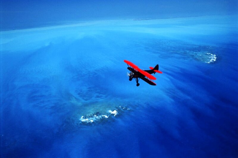 Red biplane over blue ocean