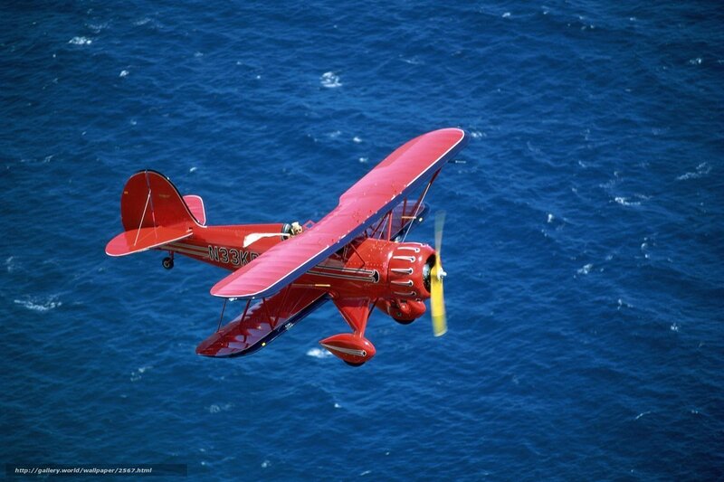 Red biplane over blue ocean