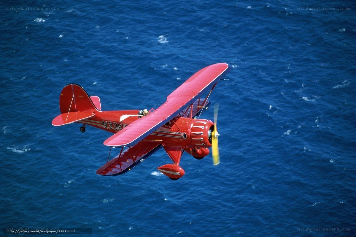 Red biplane over blue ocean