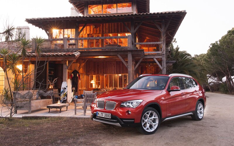 Red BMW X1 in front of wooden house