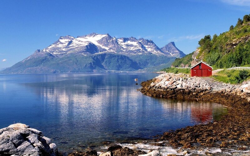 Red cabin by fjord with mountains