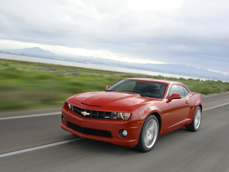 Red Camaro driving on coastal road