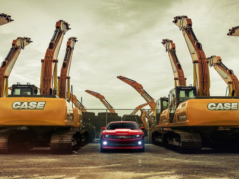 Red Car Between Excavators — Dramatic
