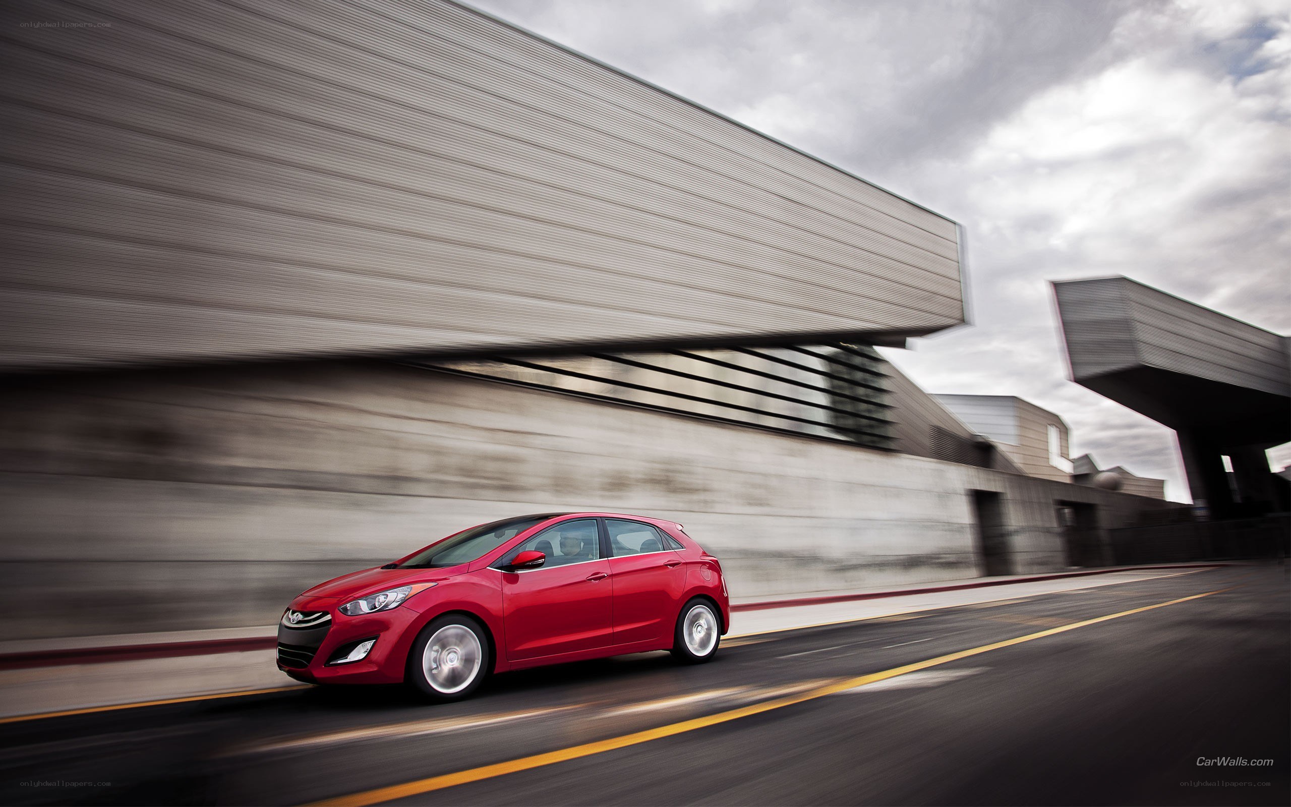 Red car driving past modern building