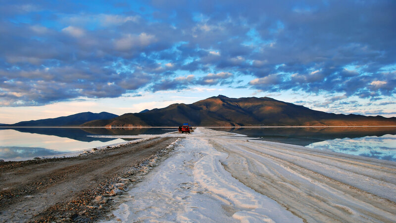 Red car on salt flat at sunset