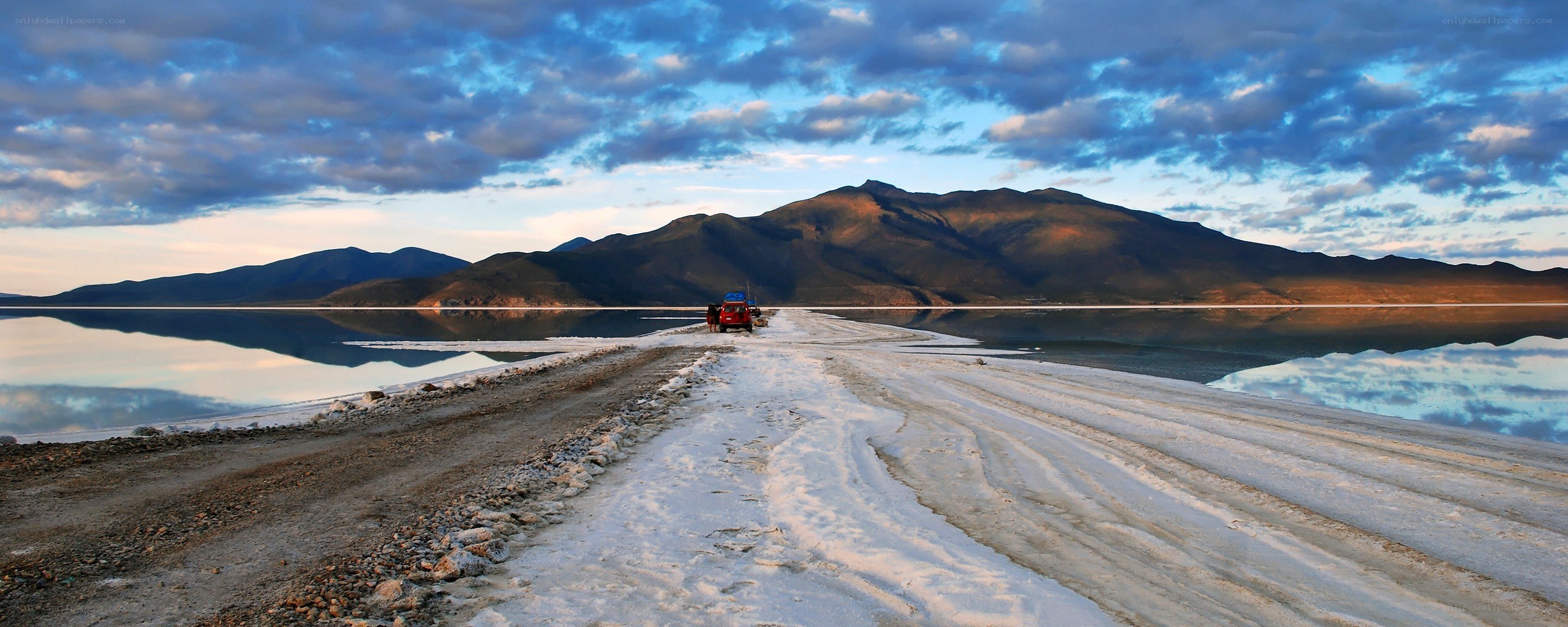 Red car on salt flat at sunset
