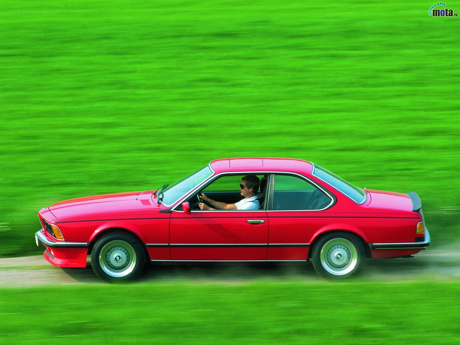 Red coupe driving on green field