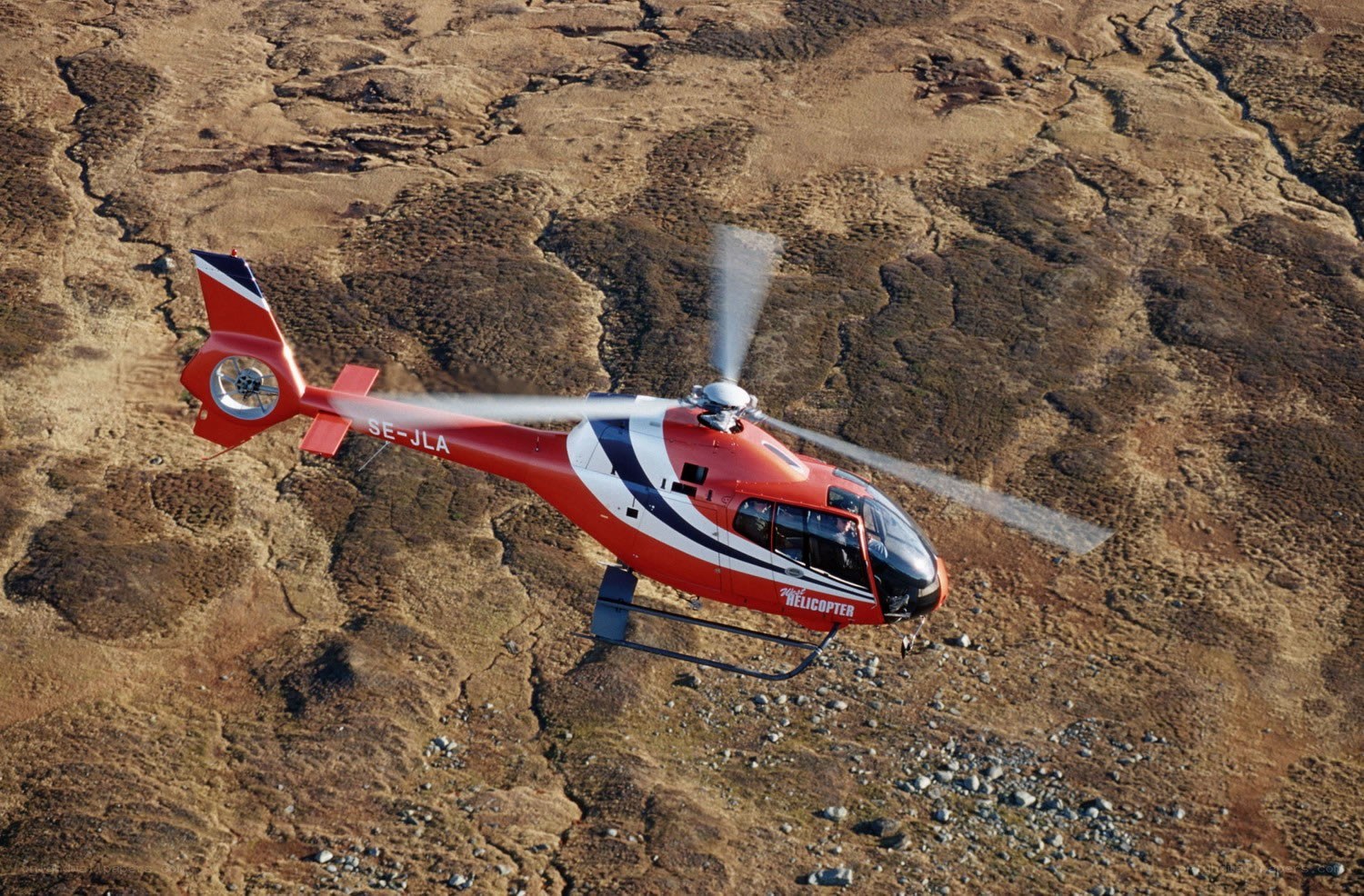 Red helicopter flying over rugged terrain