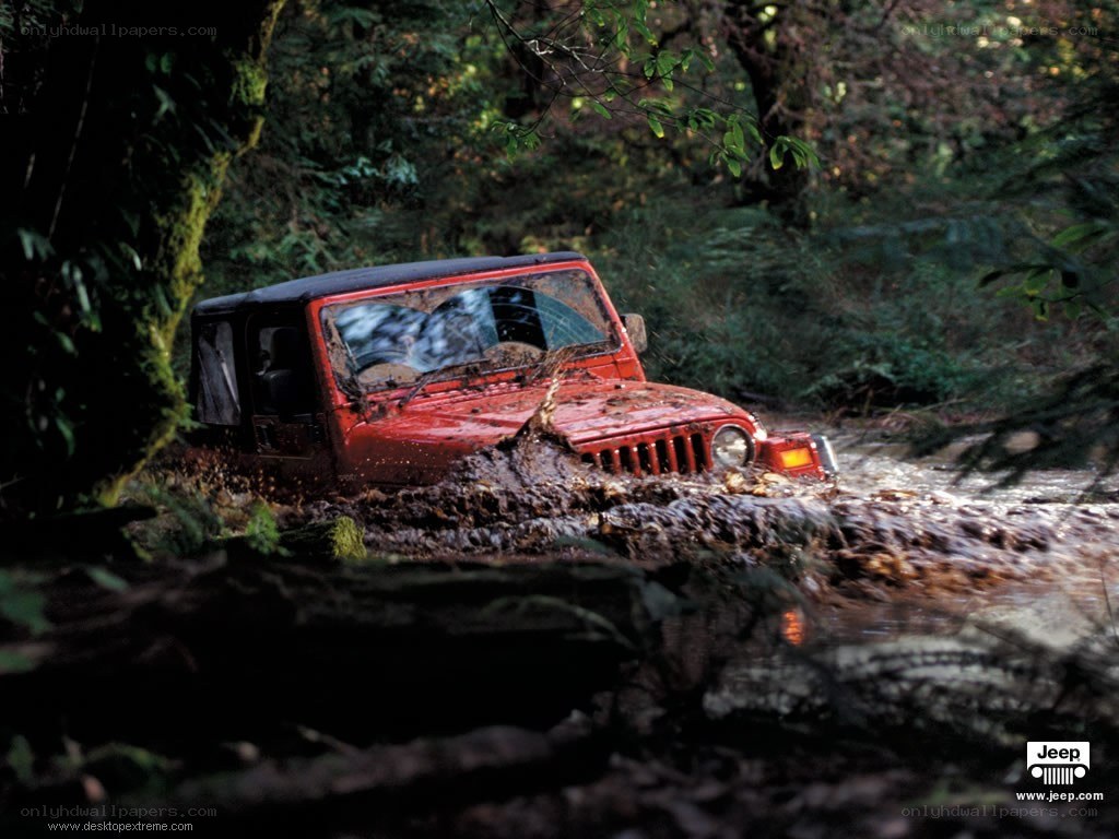 Red jeep driving through mud