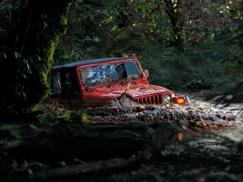 Red jeep driving through mud