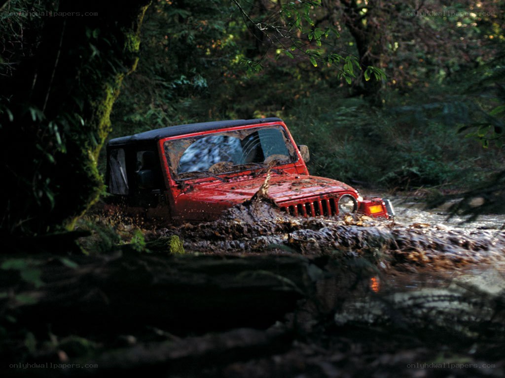 Red jeep driving through mud