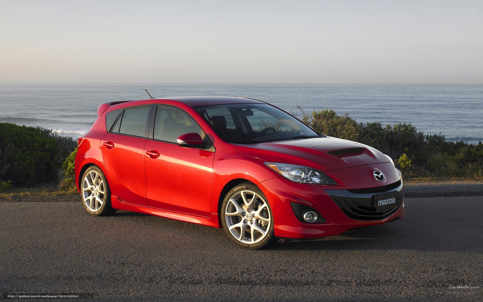 Red Mazda 3 hatchback by the sea