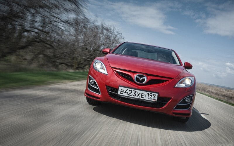 Red Mazda driving on road