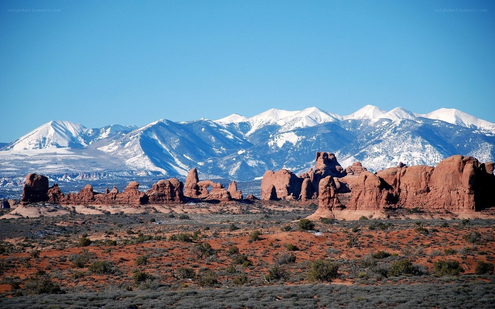 Red rock formations with snow-capped mountains