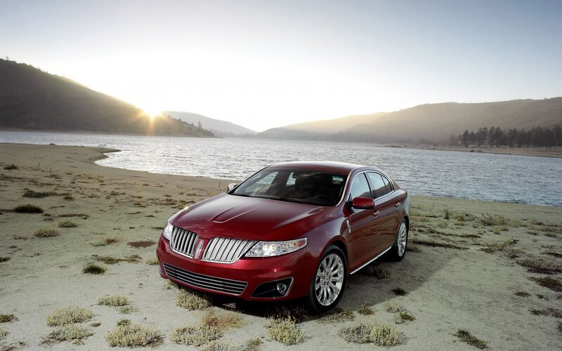 Red sedan by a lake at sunset