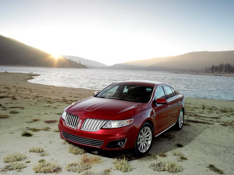 Red sedan by a lake at sunset