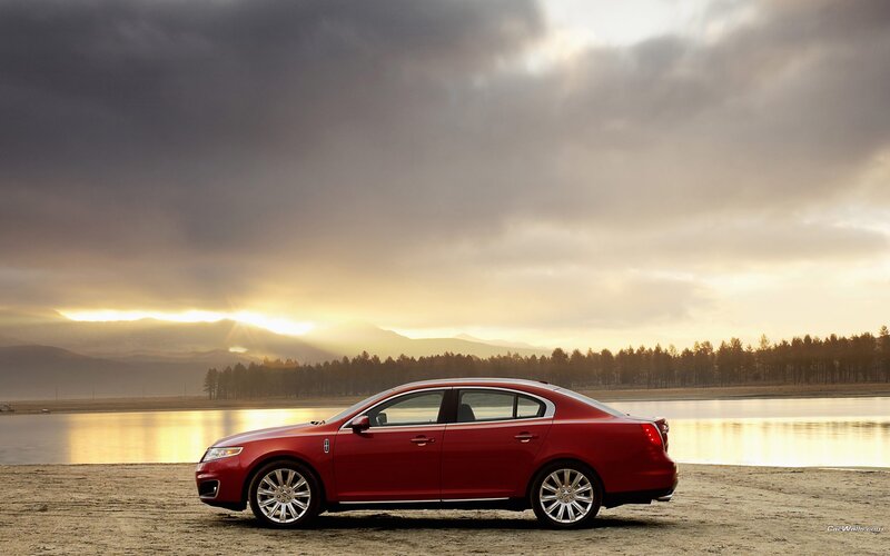 Red sedan by a lake at sunset