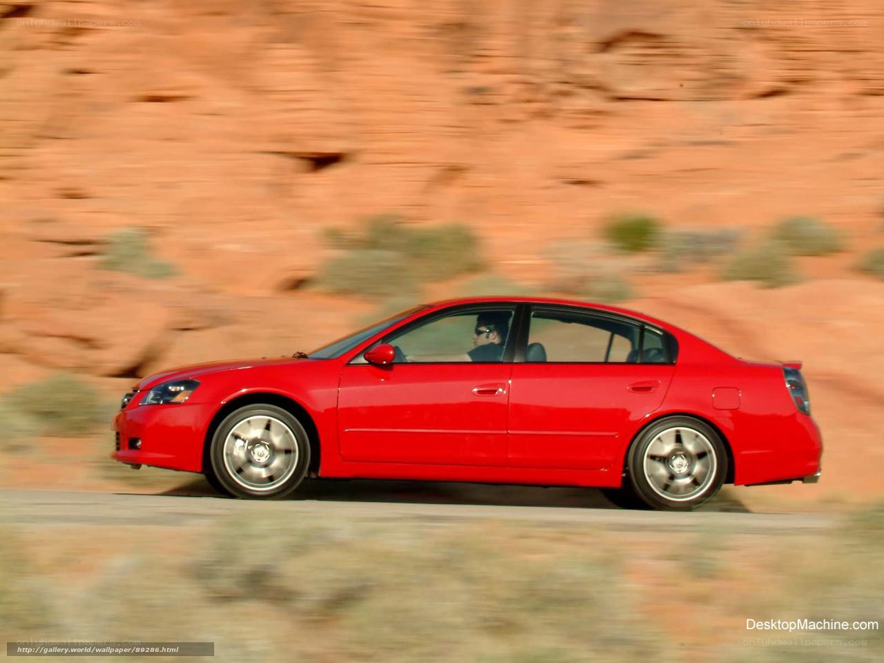 Red sedan driving on desert road