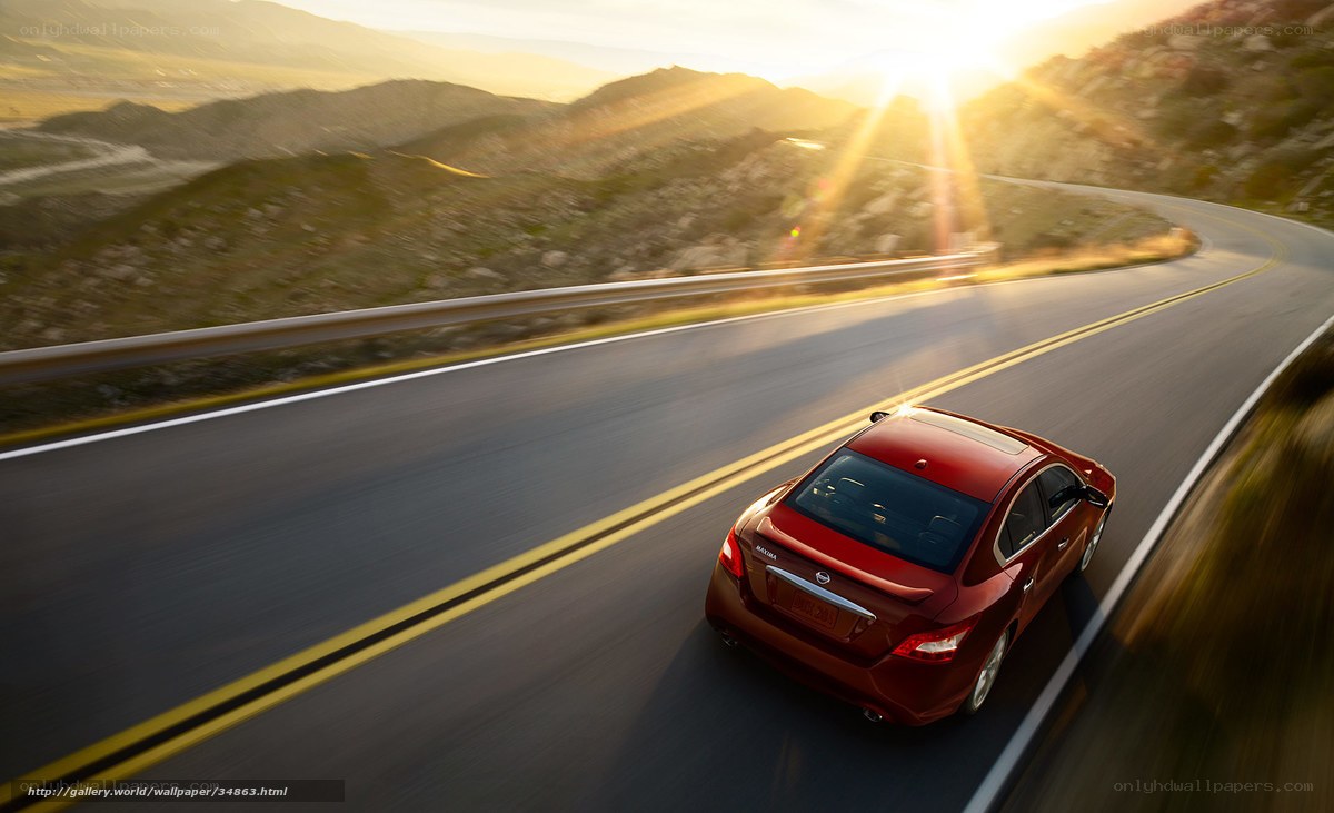 Red sedan on winding road at sunset