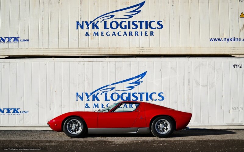 Red sports car in front of shipping containers