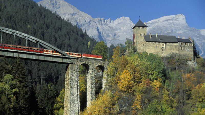 Red train crossing bridge near castle
