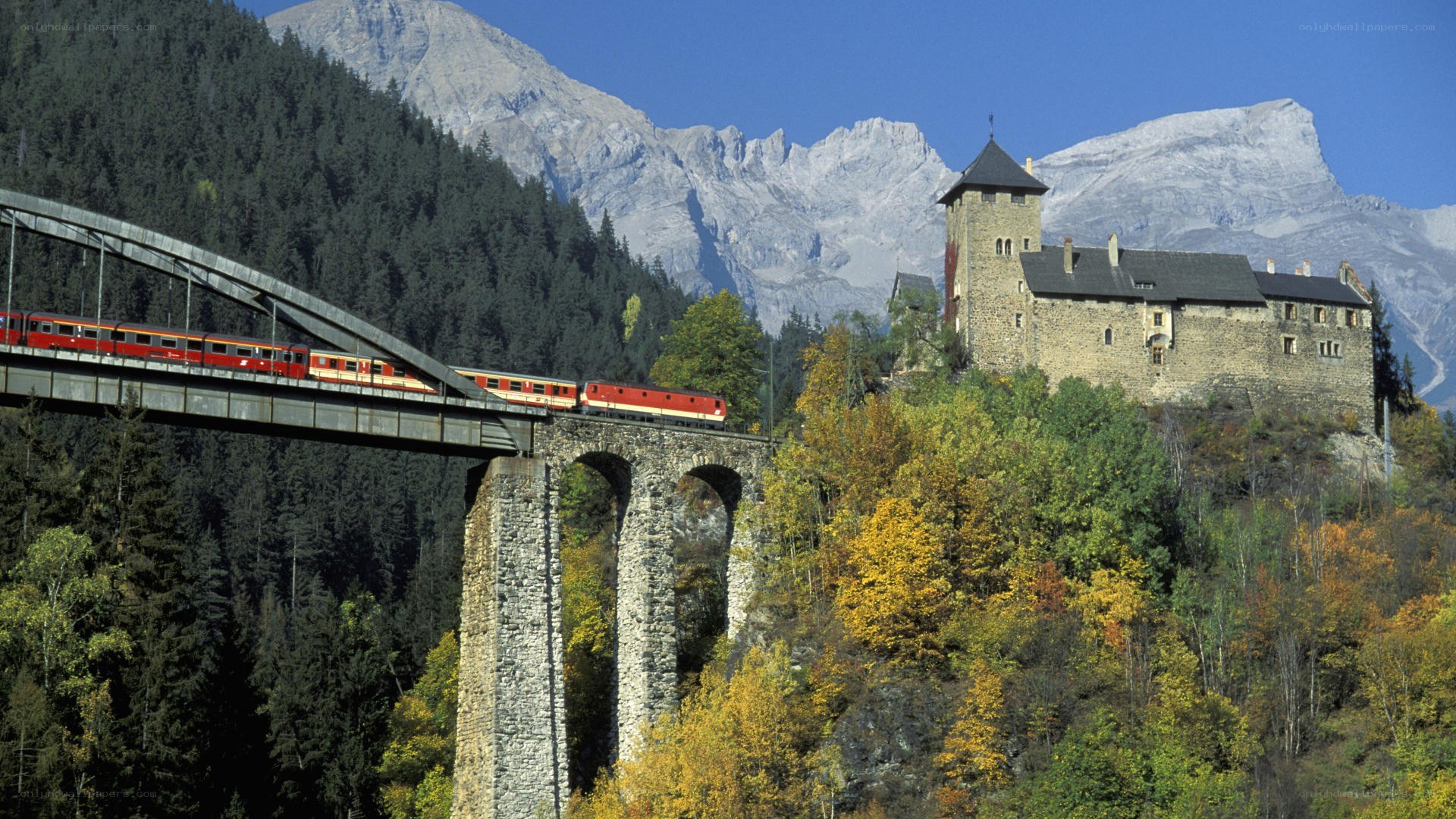 Red train crossing bridge near castle