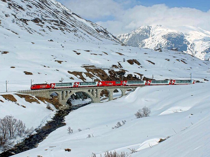 Red train crossing snowy bridge