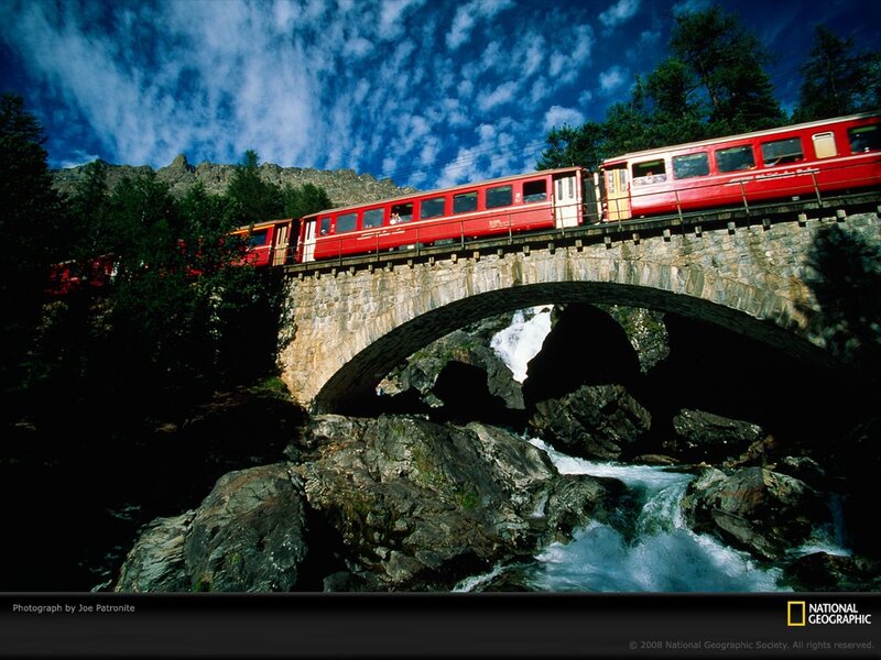 Red train crossing stone bridge