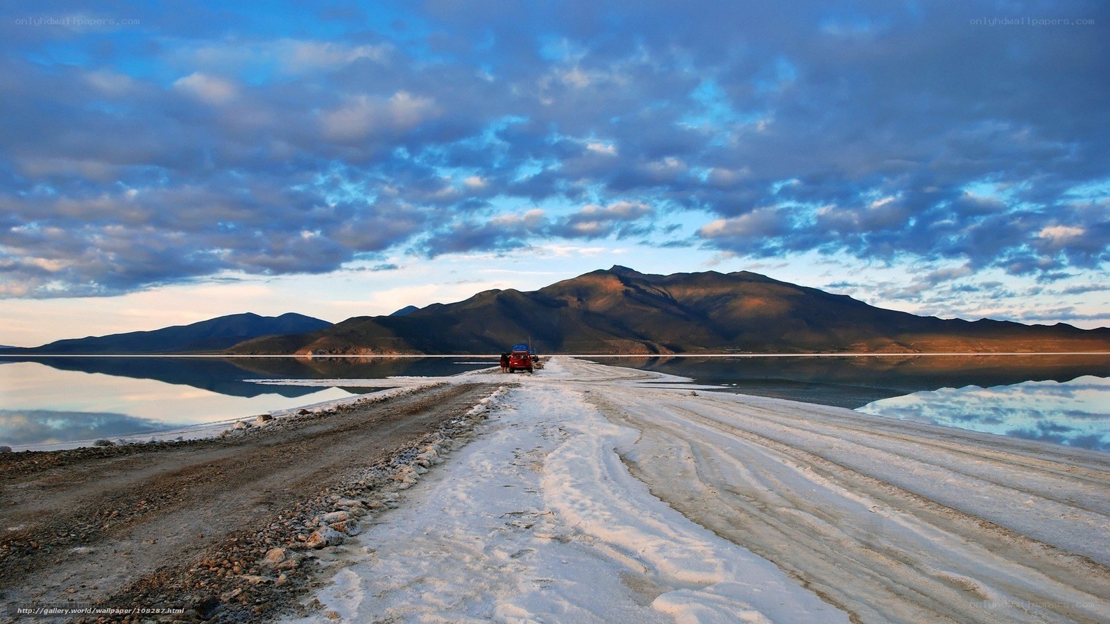 Red vehicle on salt flat at sunset