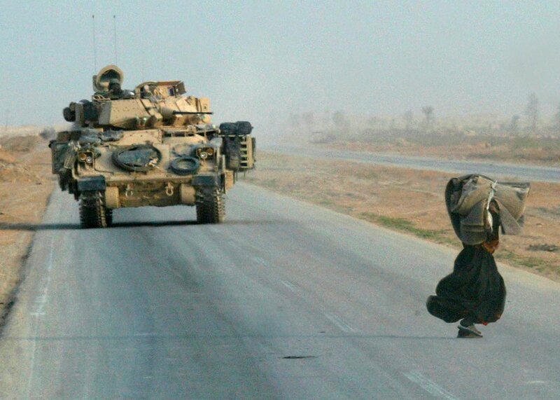 Refugee walks past military vehicle