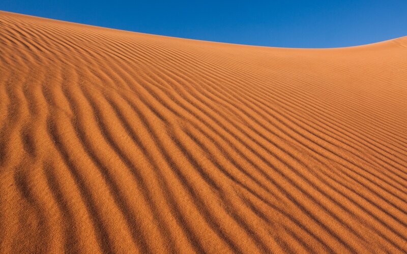 Rippled sand dunes under blue sky
