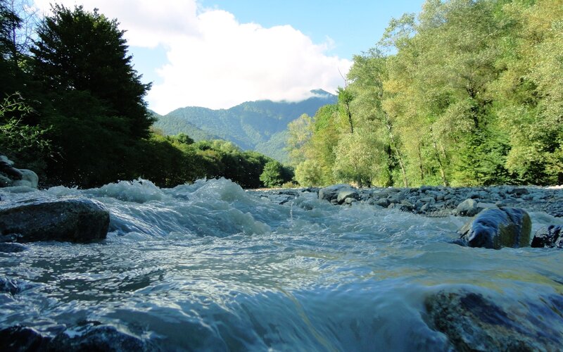 River Flowing over Rocks — Green, Serene, Afternoon, Photograph, Trees, Mountains, Sky