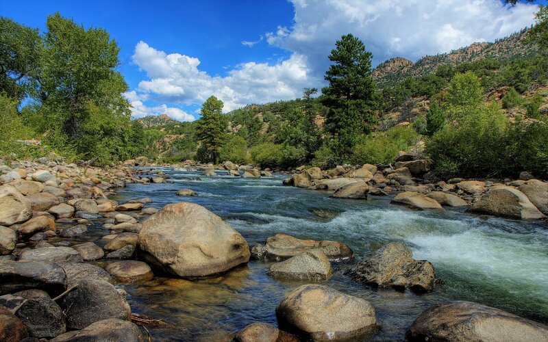 River Flowing Through Rocks — Blue, Serene, Afternoon, Photograph, Trees, Mountains, Sky