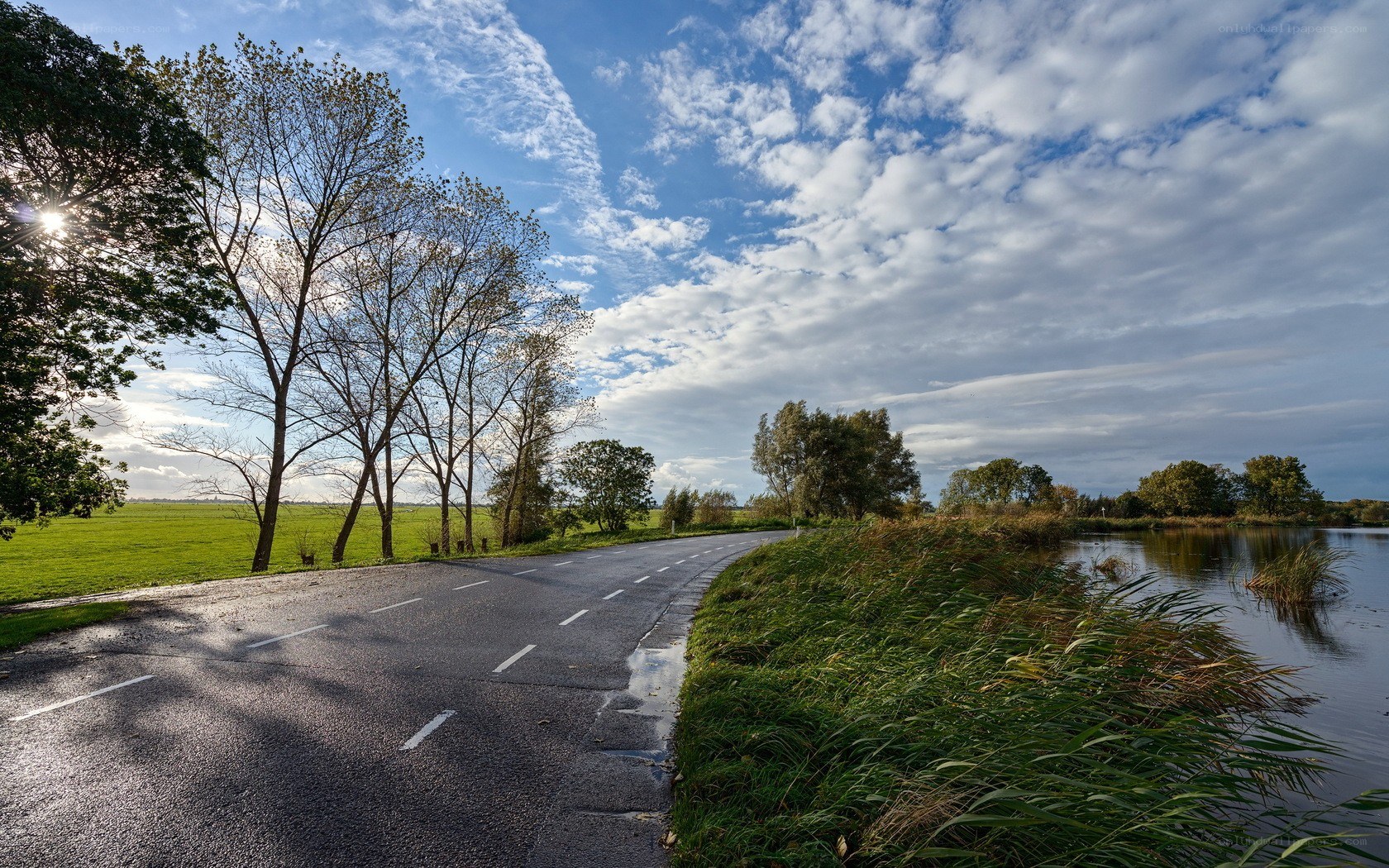 Road beside a canal under cloudy sky