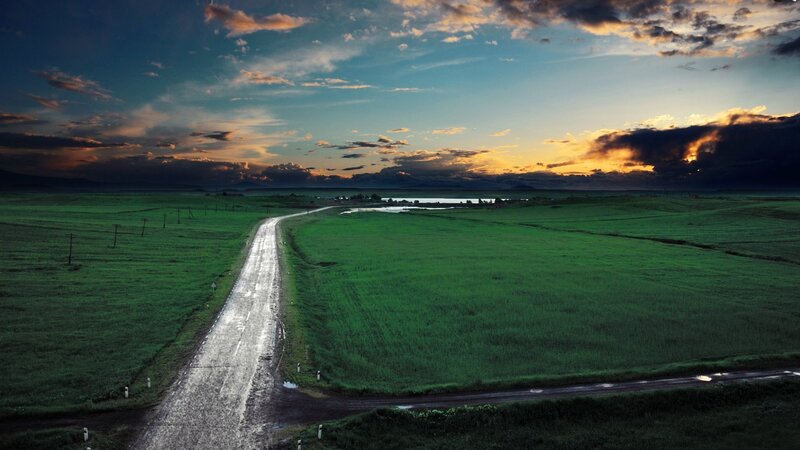Road through green fields at sunset