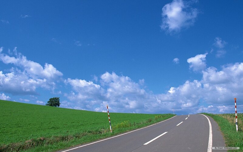 Road through green fields under blue sky