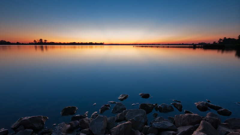 Rocks on Lake Shore — Blue, Serene, Sunset, Photograph, Sky, Trees, Orange