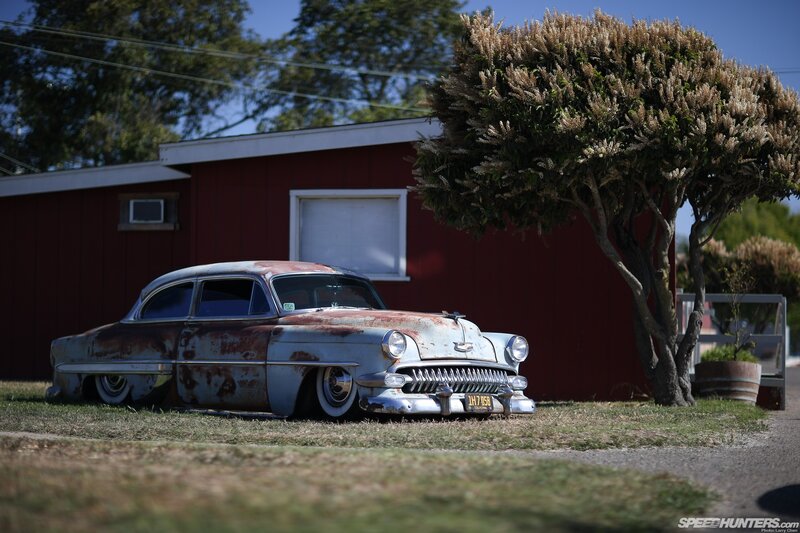 Rusty classic car in front of red building